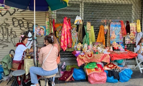 Three women sit around a small table next to a stall selling holy statues and other items