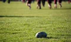Rugby ball on playing field, rugby players in  background.
