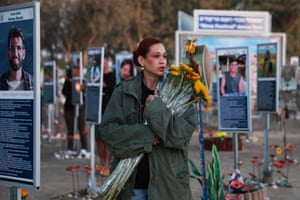 A woman holding a bunch of flowers at a memorial site with posters of victims