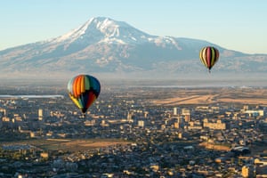 Brightly coloured balloons over an urban landscape on a sunny day, with a snow-capped mountain in the distance