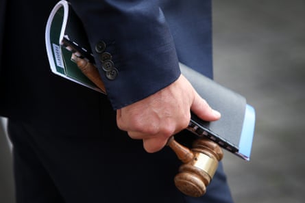 Picture of a man in a suit holding a gavel and a folded binder