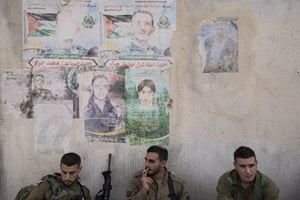 Israeli soldiers rest next to faded posters of slain Palestinian fighters