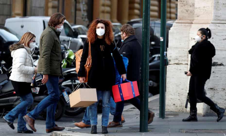 People wearing face masks walk down a street in Rome.