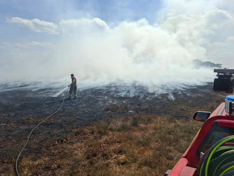 A firefighter sprays water onto burnt ground.