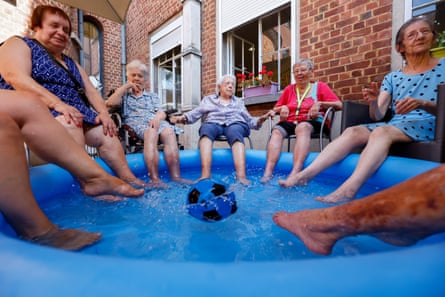 A group of elderly women at a care home sit with their feet in a paddling pool.