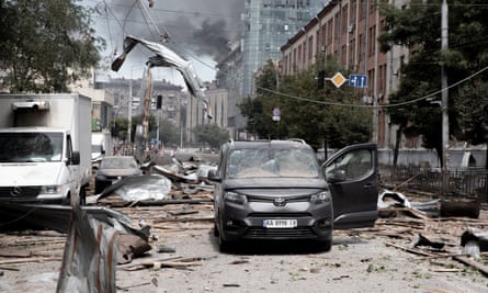 Smoke rising in the background on street with damaged buildings and cars
