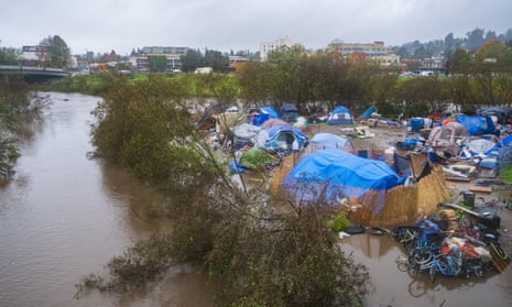 A homeless encampment filled with tents sits in floodwater from a swollen river.