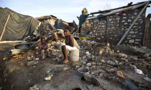 A woman and a child sit on a buckets amid the ruins of their home in Jeremie