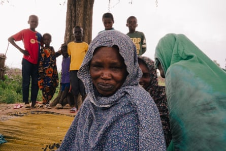 An older woman looks at the camera with a grim smile while children stand in the background
