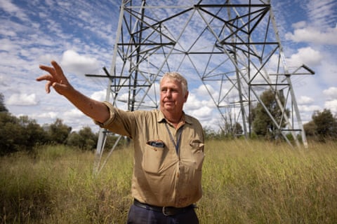 Middle aged man standing in grassland with a high voltage power line tower behind him