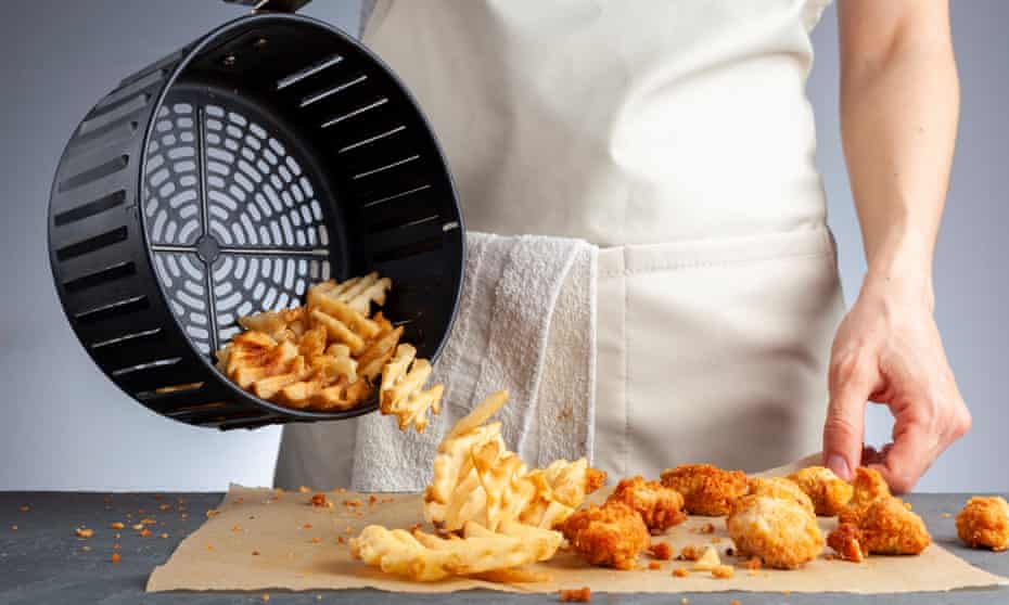 Air frying waffle potato fries at home. A woman is dumping fresh made potato waffle fries from basket onto a countertop together with chicken nuggets