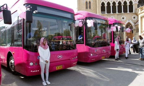 Three pink buses parked in a row. Young woman dressed in white and wearing pink hijab stands in front of the nearest bus