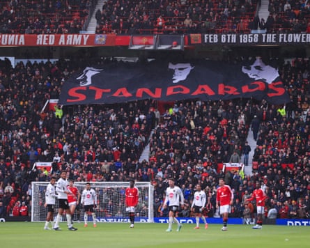 Manchester United fans at Old Trafford hold up a large black banner featuring black-and-white images of Bryan Robson, Roy Keane and Eric Cantona and bearing the word ‘Standards’ in large red letters.