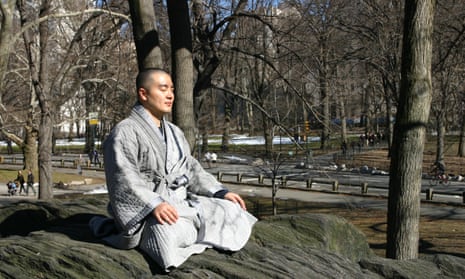 Haemin Sunim sitting cross-legged, meditating, in a park wearing a grey robe
