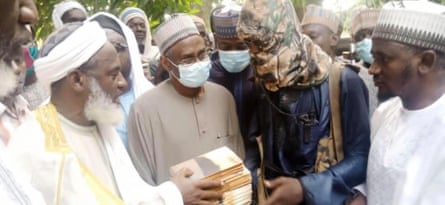 A Muslim cleric handing books to a masked man