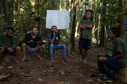 A group of men sit in a clearing in a jungle
