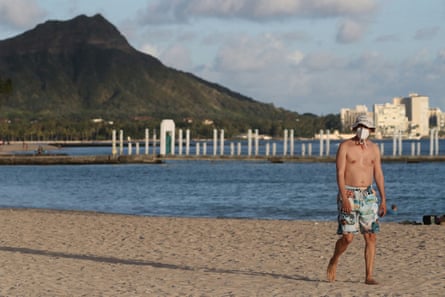 A beachgoer wears a mask on Waikiki beach in Hawaii, with Diamond Head mountain in the background.