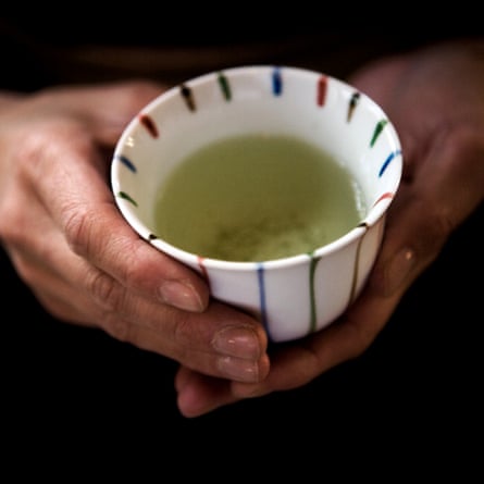 A cup containing fresh brewed green tea held within two hands.