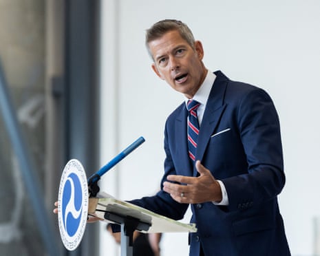man in blue suit speaks at lectern marked with 'department of transportation' with hand gestured