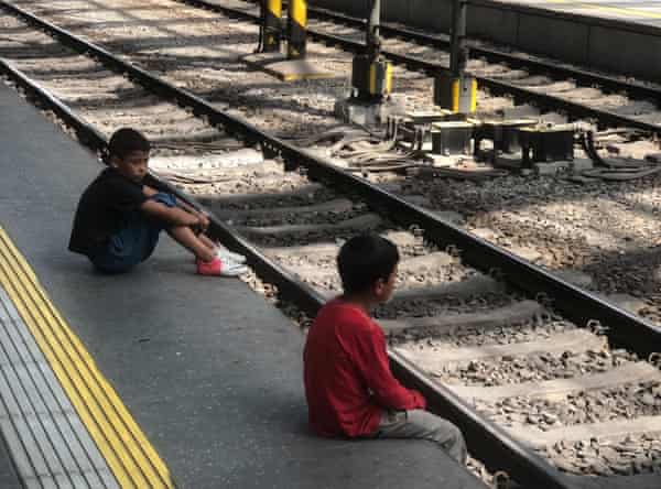 Two young boys are sitting at the edge of a station platform