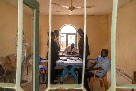 A group of people sit a table in a dilapidated room.