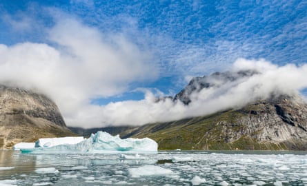 An icy sea, with mountains and clouds behind, under a blue sky