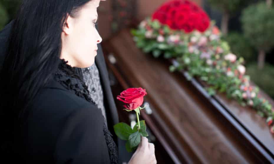 A woman standing over a coffin with a rose in her hand