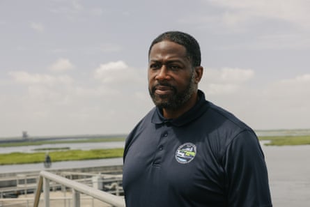 man in collared shirt stands outside by water looking ahead