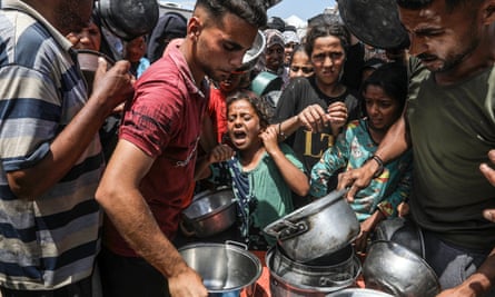 A young girl cries in the middle of a crowd of people with large saucepans