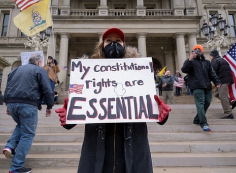 A woman wearing a face mask holds a placard as supporters of the Michigan Conservative Coalition protest against the state’s extended stay-at-home order.