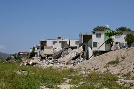 A house by what looks like a dry riverbed that has half-collapsed