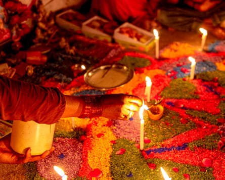 A person lights candles on a brightly coloured floor during Diwali