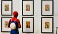 A figure dressed as Spider-Man gazes at framed comic covers including Fantastic Four, at an exhibition on Stan Lee