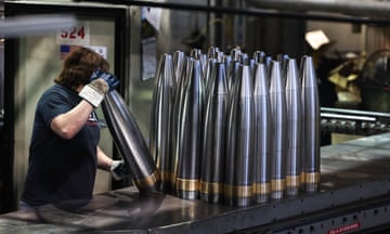 A woman handles steel tubes with brass rings in an armaments factory