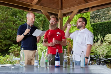 They stand in a wooden gazebo, behind a table of bottled water. Usborne is reading from a menu