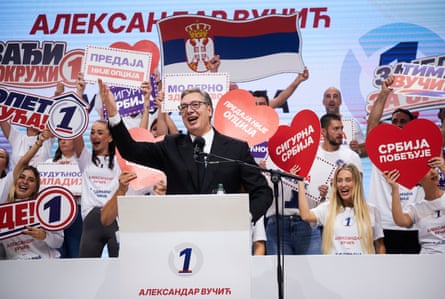 Aleksandar Vučić speaks at a rally podium, surrounded by cheering supporters holding heart-shaped signs