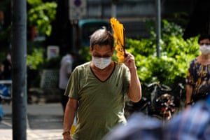 A man wears face mask and uses a fan to block the sun walks on a street in Hong Kong, China.