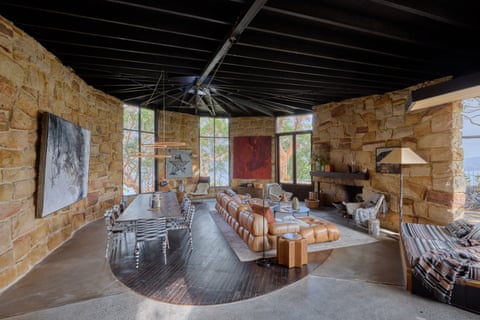 A large slightly curved room with a dining table behind a lounge facing a fireplace and wall.