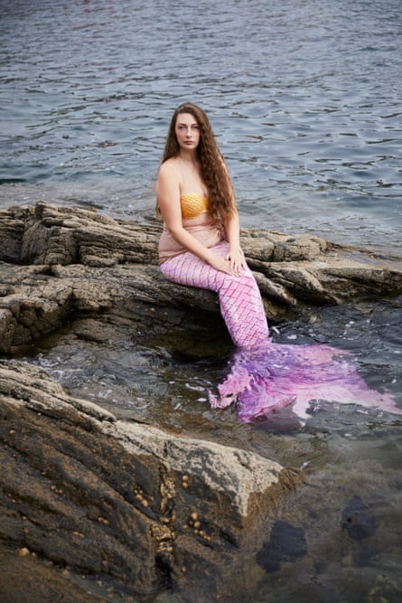 Tasha Fairey as a mermaid with a pink tail, sitting on rocks in water