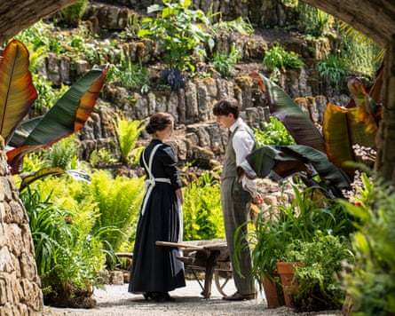 Two people standing under a brick archway with lush plants around them
