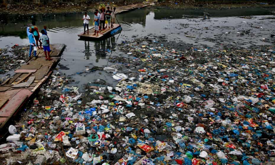 A man punts a raft across a canal in Mumbai, India, that is clogged with plastic waste