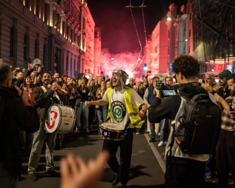 A student drummer shouts joyfully as crowds welcome them in Belgrade at night