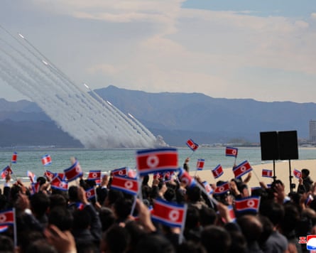 North Korean rocket launchers fire over the sea as a crowd waves flags