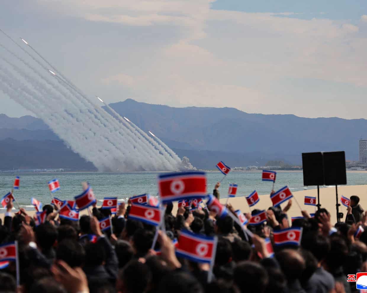 North Korean rocket launchers fire over the sea as a crowd waves flags