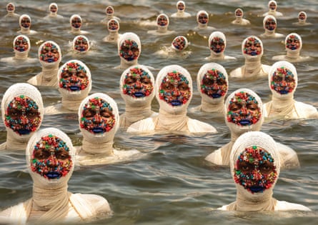 Repeated images of a woman wrapped in bandages with flowers stuck to her face standing up to her shoulders in water