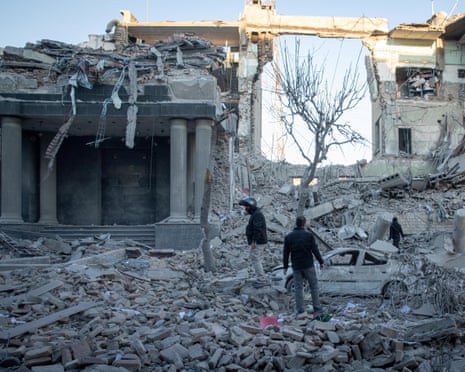 people standing in rubble after an airstrike