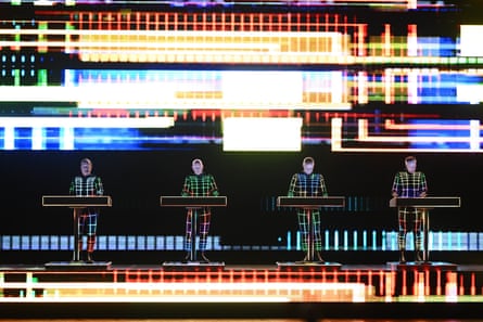 Kraftwerk standing at four podiums wearing futuristic costumes with neon graphics behind them