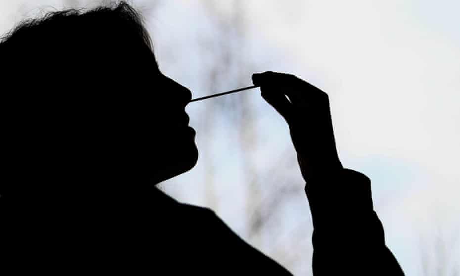 A silhouette of a person swabbing their nose for a Covid-19 rapid antigen test
