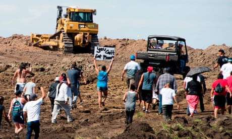 people protest at a construction site, one person holding a sign saying 'you can't eat money'