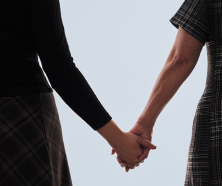 Back view of two women, from shoulders down, holding hands